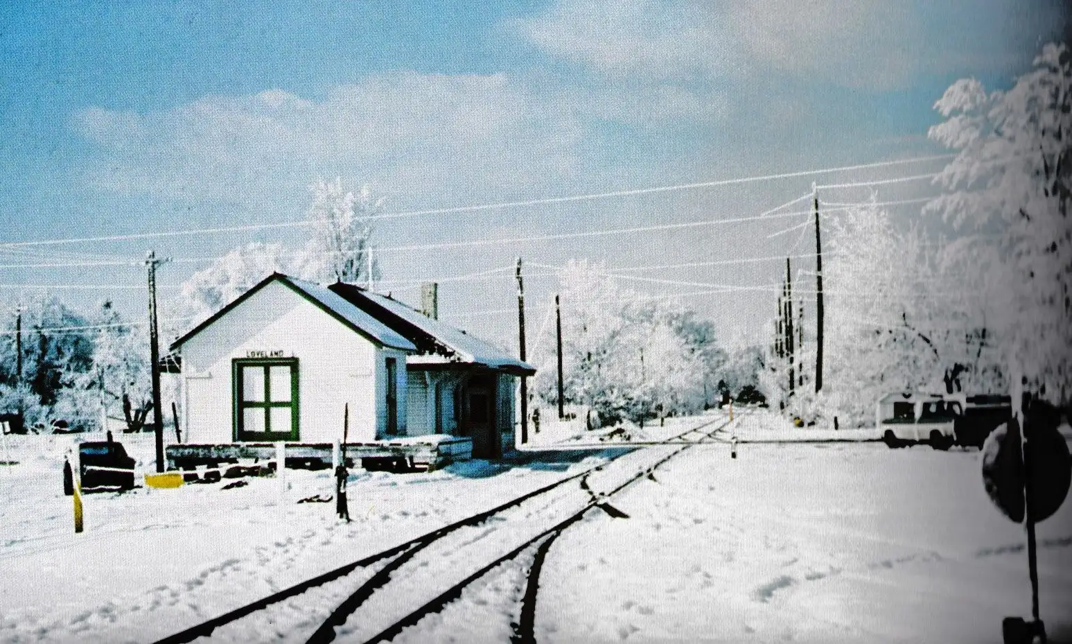 Photo of white train depot building next to train tracks, snow on the ground and in the trees
