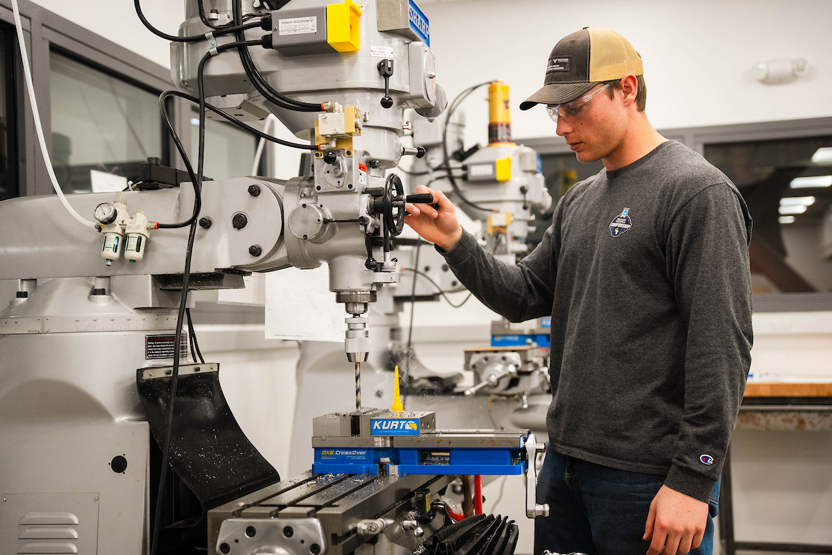 A person operates a CNC milling machine in a workshop, adjusting settings with a handwheel.